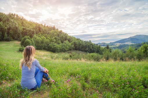 Girl sitting on a green meadow and watching the countryside landscape.