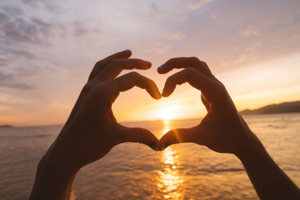 istock Hands and fingers in heart shape framing setting sun at sunrise over ocean 845307712