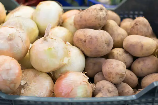 Potatoes and onions in the market inside a plastic basket.