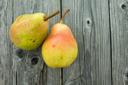 Two ripe red yellow pear fruits with green leaves, on wood background