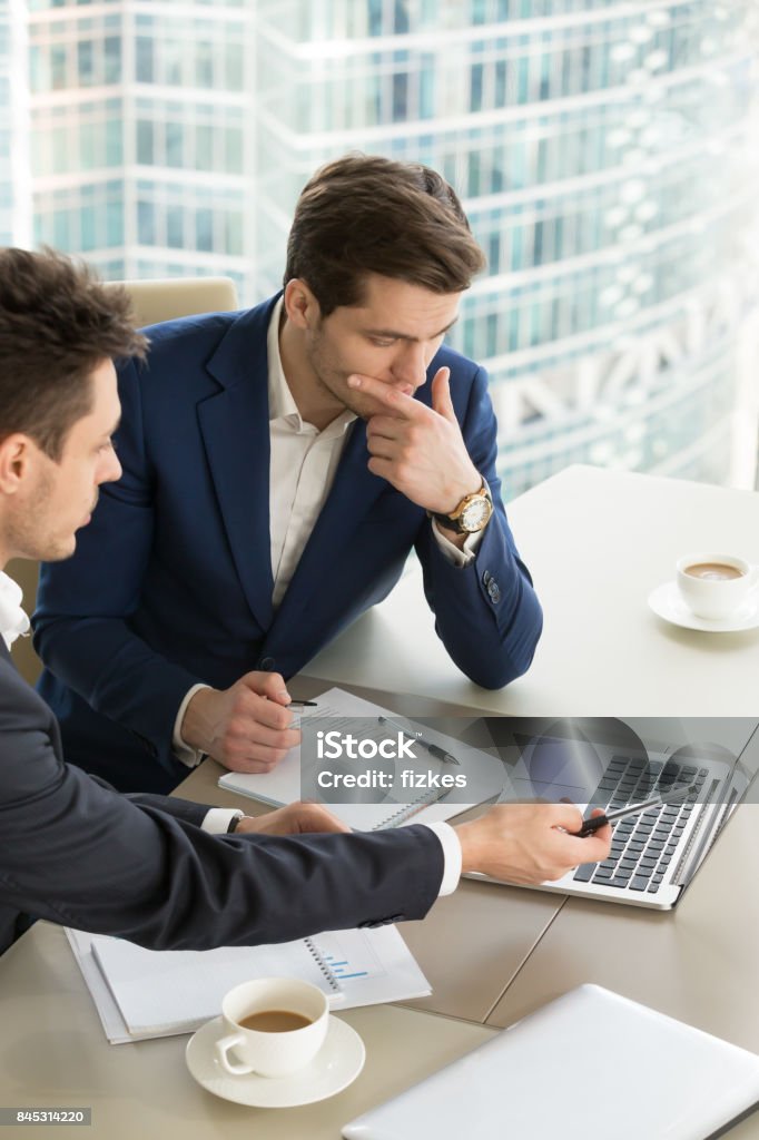 Entrepreneurs discussing work results on meeting Business partners using laptop while working together on important corporate project in office. Businessman attentively listening to adviser Investment specialist making presentation of promising deal Discussion Stock Photo