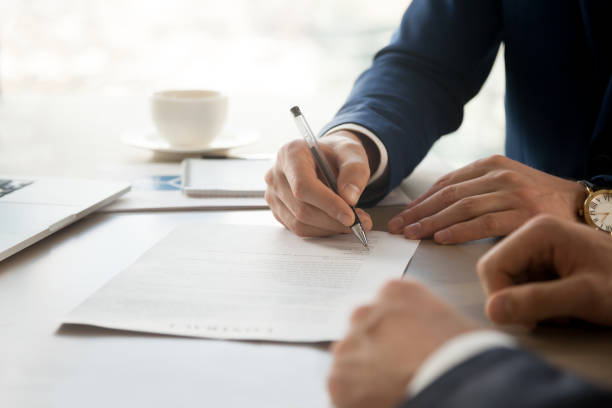 Businessman accepting business partners offer Close up image of businessman hand putting personal signature on contract document in presence of business partner. Starting successful partnership with entrepreneur or companie, making good deal banking document stock pictures, royalty-free photos & images