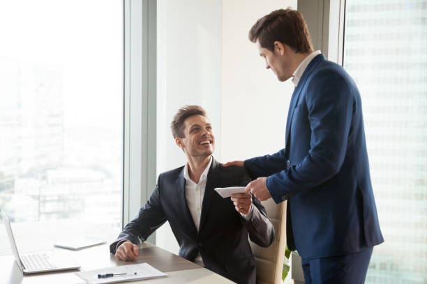 Boss giving money premium to happy employee General manager presenting an envelope with premium or bonus cash to male company official. Boss congratulating happy employee with career promotion, thanking for good job and giving financial reward professional thank you stock pictures, royalty-free photos & images