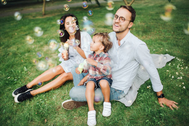 Happy young family playing with bubble wands in park outdoors stock photo
