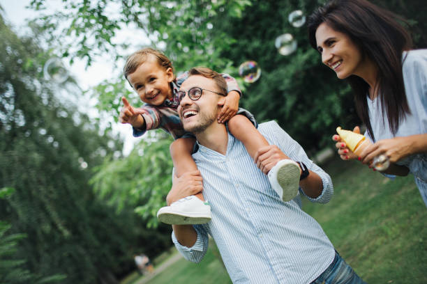 Happy young family playing with bubble wands in park outdoors stock photo