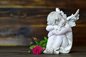 Sleeping angel and single rose on wooden background