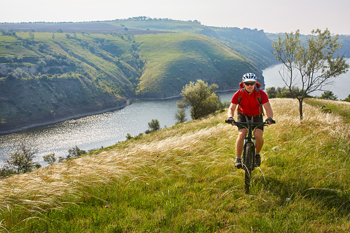 Adventure mountain biking on riverside. Traveler with backpack rides his bike in mountains.