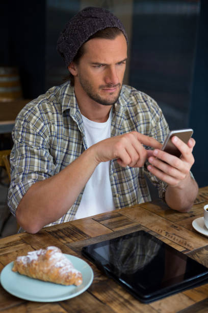 hombre guapo con teléfono móvil en la mesa en la cafetería - croissant telephone coffee shop on the phone fotografías e imágenes de stock
