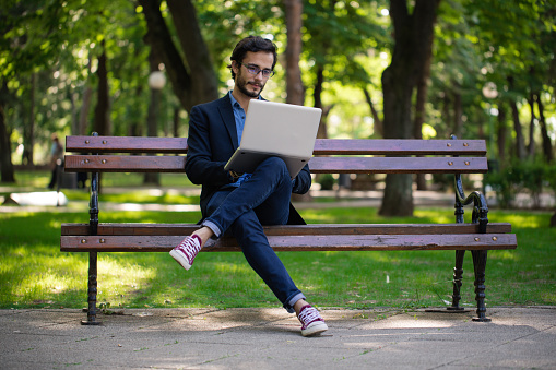Young businessman sitting in the park and using laptop