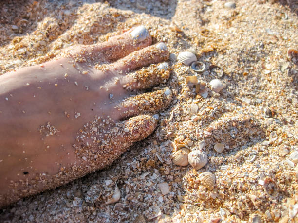 istock Women's foot with painted silver fingernails. Leg standing on the sand. Pedicure 845358432