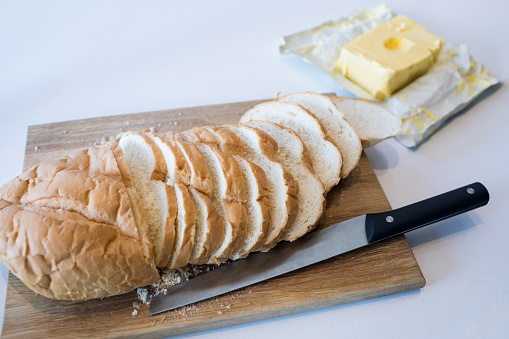 Slice of bread on chopping board with knife and butter in kitchen worktop at home