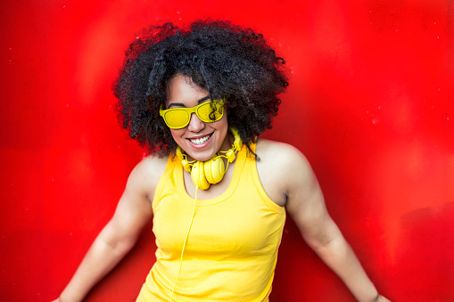 Woman wearing yellow vest, vest and sunglasses in front of red background
