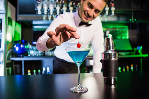 Bartender garnishing cocktail with cherry on bar counter in bar