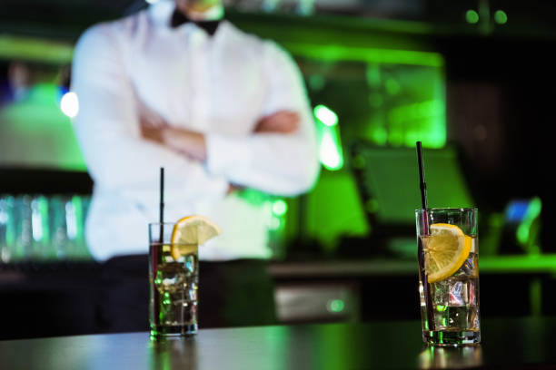 Two glasses of gin on bar counter and bartender standing in background