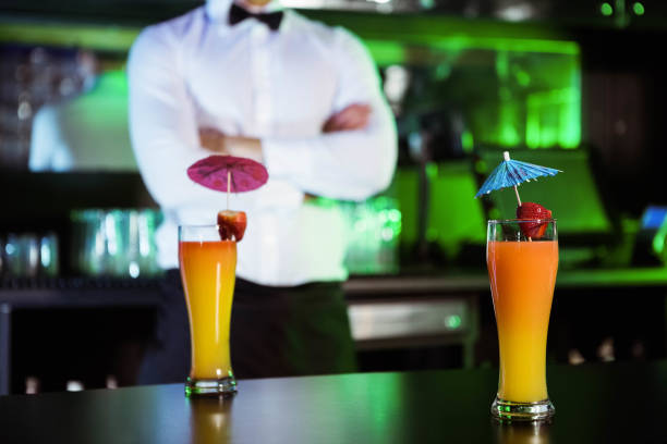 Two glasses of cocktail on bar counter and bartender standing in background