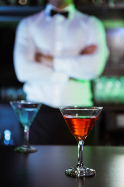 Two glasses of cocktail on bar counter and bartender standing in background