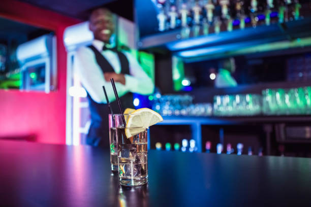Two glasses of gin on bar counter and bartender leaning in background