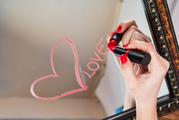 Girls hand with red lipstick drawing heart and word love on mirror for Valentines day Girls hand drawing with red lipstick heart and word love on mirror for Valentines day mirror writing stock pictures, royalty-free photos & images