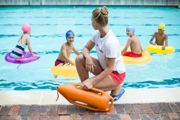 Female lifeguard holding rescue can while children swimming in pool