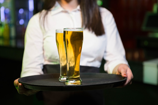 Bartender serving two glasses of beer in bar