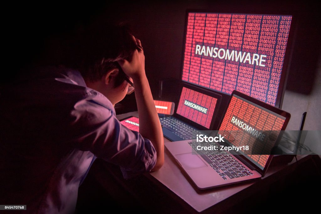 Young Asian male frustrated by ransomware cyber attack Young Asian male frustrated, confused and headache by ransomware attack on desktop screen, notebook and smartphone, cyber attack and internet security concepts Ransomware Stock Photo