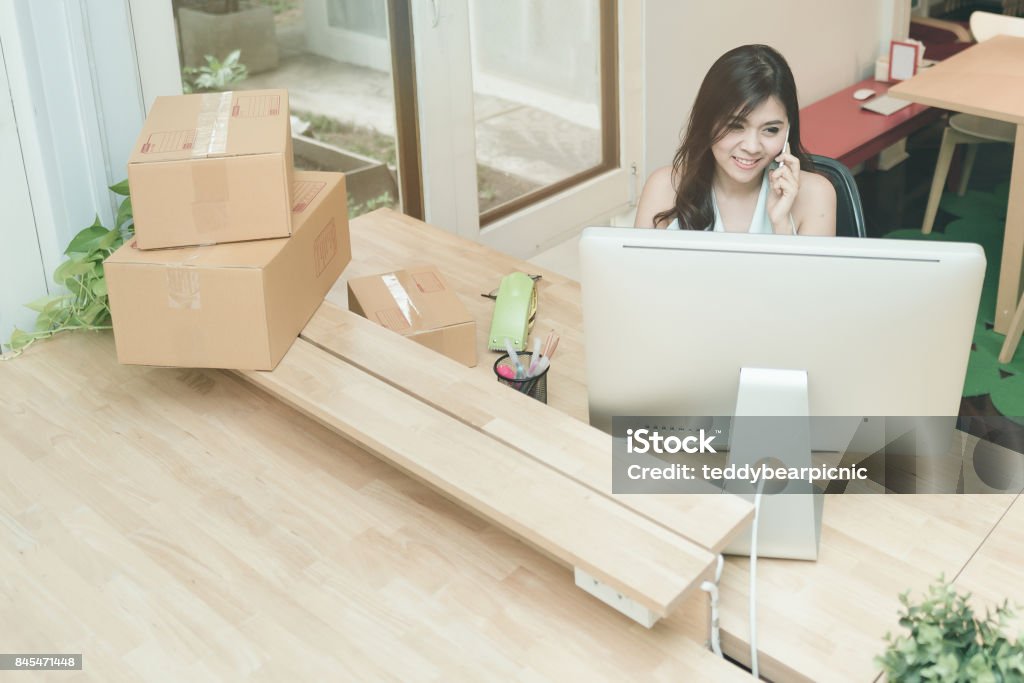 Young entrepreneur working on the smart computer while talking to her customer at home office. Young entrepreneur working on the smart computer while talking to her customer at home office.Conceptual for small businesses starting own company and online marketing. Adult Stock Photo