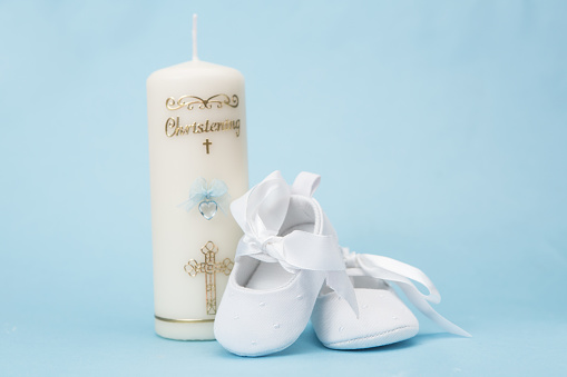 Christening candle for a boy with white baby booties on blue background