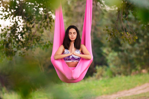 Aerial antigravity yoga. Young healthy women doing lotus pose on silk hammock at nature stock photo