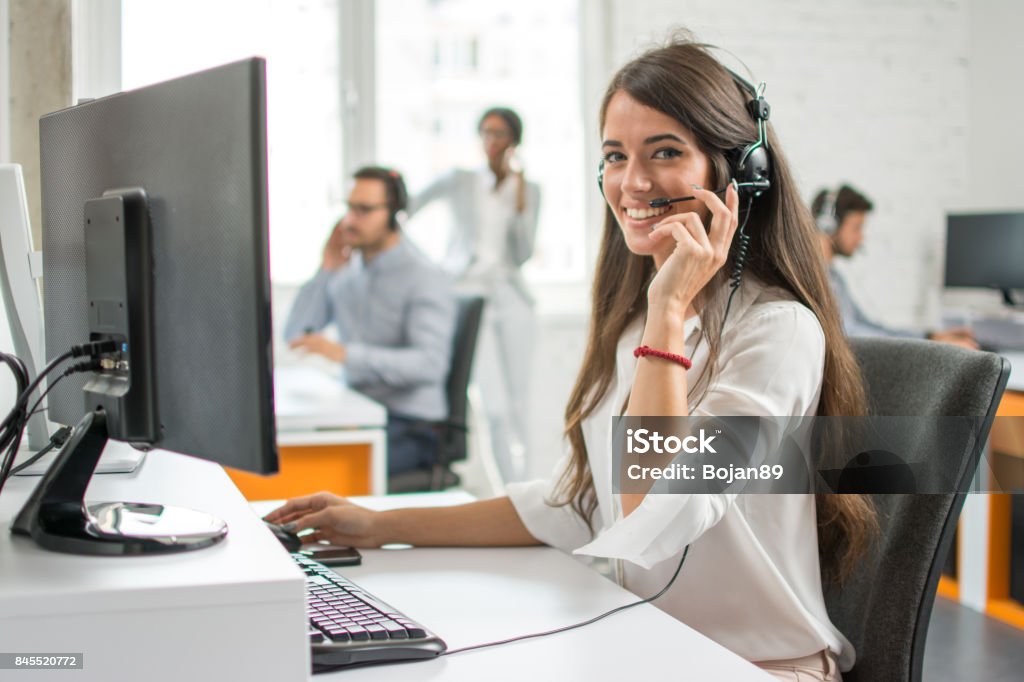 Agente de mulher jovem operador amigável com fones de ouvido trabalhando em um call center. - Foto de stock de Agente de atendimento ao cliente royalty-free
