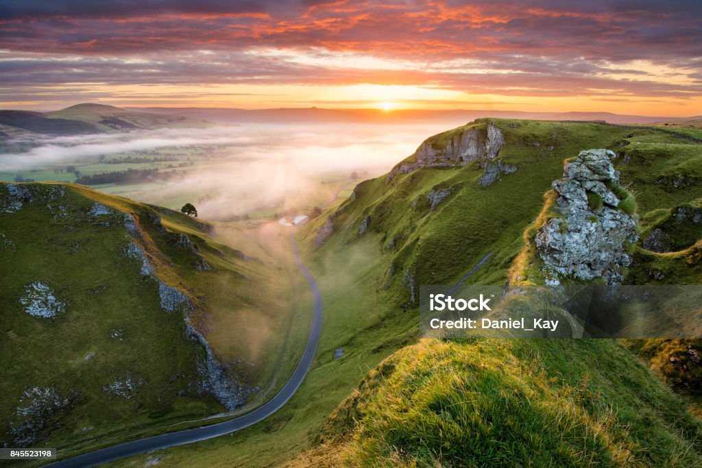 Winding Road At Sunrise In The Peak District. Long winding rural road leading into misty valley in the English Peak District. Landscape - Scenery Stock Photo