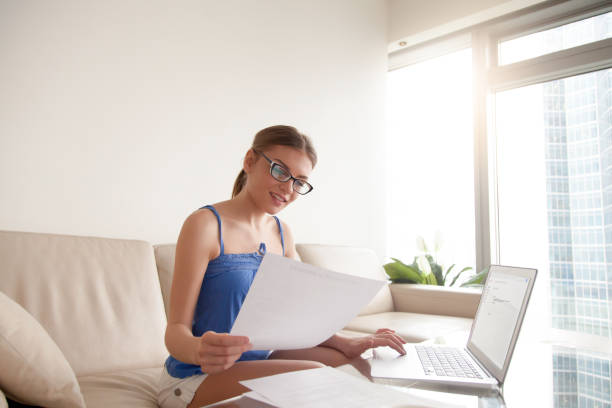 istock Young woman wearing glasses holding document using laptop at home 845527140