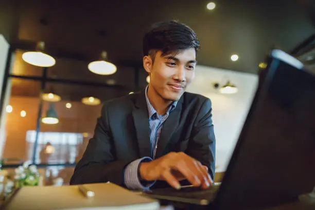 Photo of Smiling asian businessman in suit working with laptop