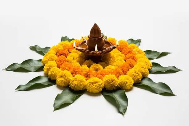 flower rangoli for Diwali or pongal or onam made using marigold or zendu flowers and red rose petals over white background with diwali diya in the middle, selective focus