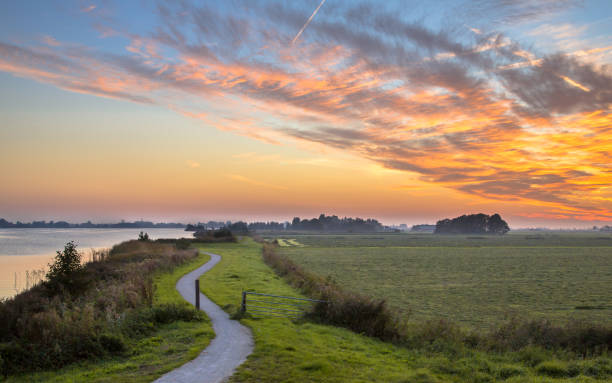 Polder landscape with winding cycling track Dutch Polder landscape with winding cycling track along river under beautiful sunset friesland netherlands stock pictures, royalty-free photos & images