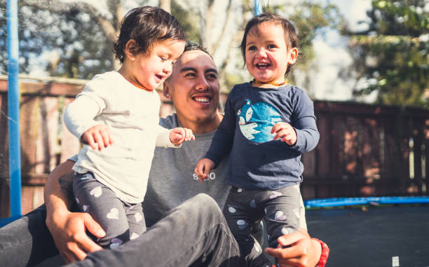 Families From New Zealand. Kids enjoying with father on trampoline. different families stock pictures, royalty-free photos & images