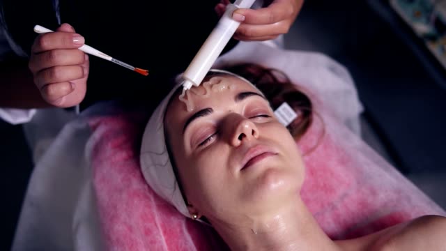 Carboxytherapy for young woman in professional spa salon. Young woman is lying on the couch while professional cosmetologist is apllying special treatment on woman's face using brush