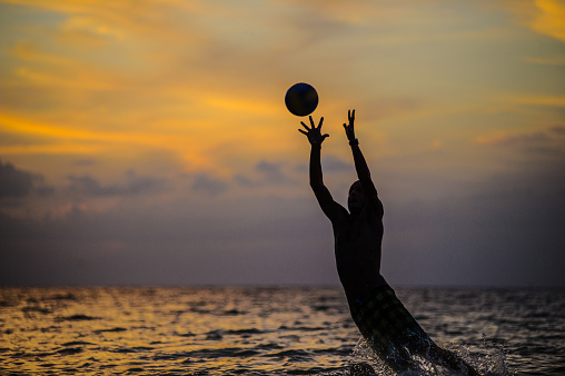 Catching a ball. Silhouette of a man jumping out of sea water.