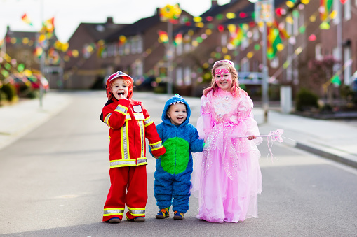 Kids on Halloween trick or treat. Children in Halloween costumes with candy bags walking in decorated city neighborhood trick or treating. Baby and preschooler celebrating carnival wearing costume.