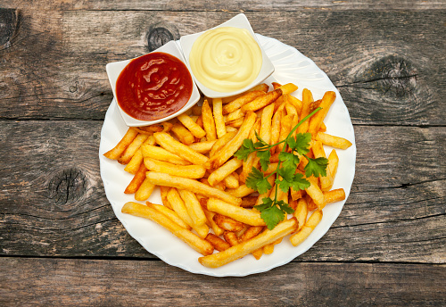 French fries on a plate with parsley, tomato sauce, salt and mayonnaise