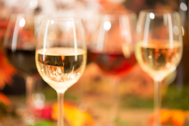 Glasses of white wine on a picnic table with flowers and food in background.