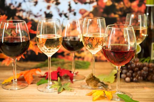 Outdoors wine tasting event in the autumn season.  Fall leaves and autumn landscape in background.  Various wines: red, white, and rose with wine bottle.  No people.