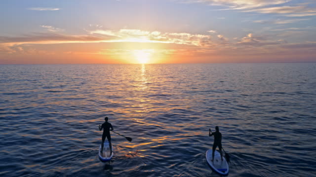 AERIAL Passing two people paddling their SUPs in Adriatic sea at sunset