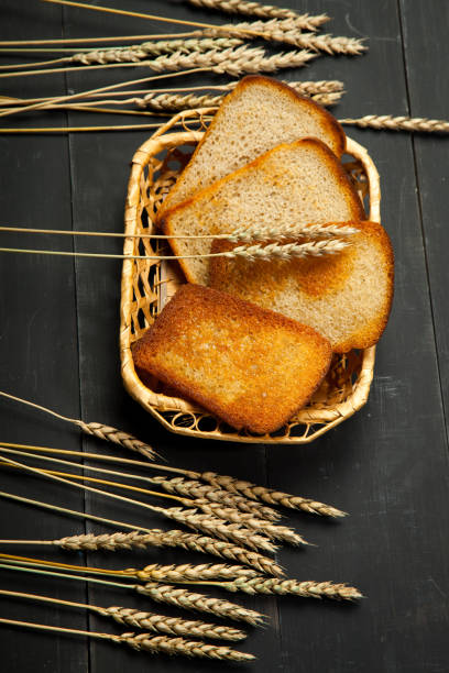 Toasts of bread and wheat on a black wooden background