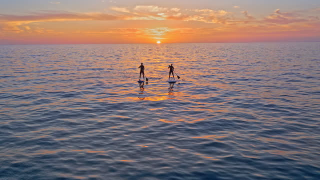 AERIAL Man and woman paddling their SUPs at sunset