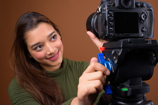 Studio shot of young beautiful Indian woman getting ready for vlogging against colored background horizontal shot