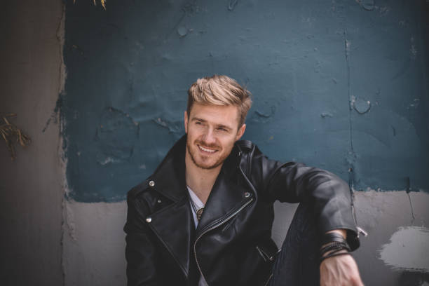Adult man in leather jacket standing against wall with no parking road sign