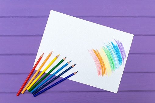 Multi-color pencils with painted rainbow on white paper on purple wooden background