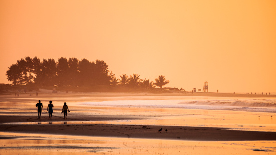 A group of young men watch the vibrant and orange sun set over moored boats from the beach of Stone Town, Zanzibar.