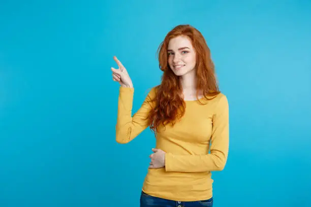 Close up Portrait young beautiful attractive redhair girl happy with something and pointing finger. Blue Pastel Background. Copy space.