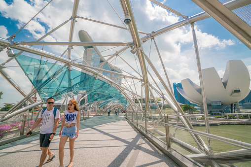 Singapore City, SINGAPORE - FEB 10, 2017: Asian tourist couple on helix bridge with Marina Bay Sands in background. Tourism in Singapore is major industry and contributor to Singapore economy.